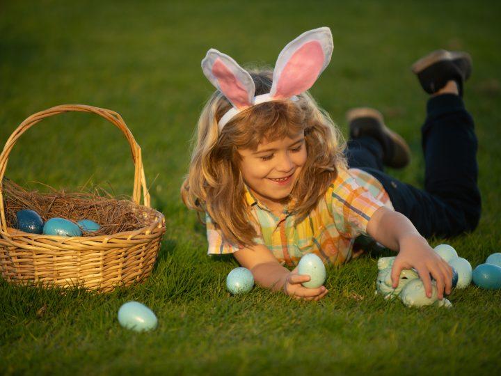 Bunny kids with rabbit bunny ears. Child boy with easter eggs and basket on grass. Child boy hunting easter eggs, laying on grass. Easter bunny children.